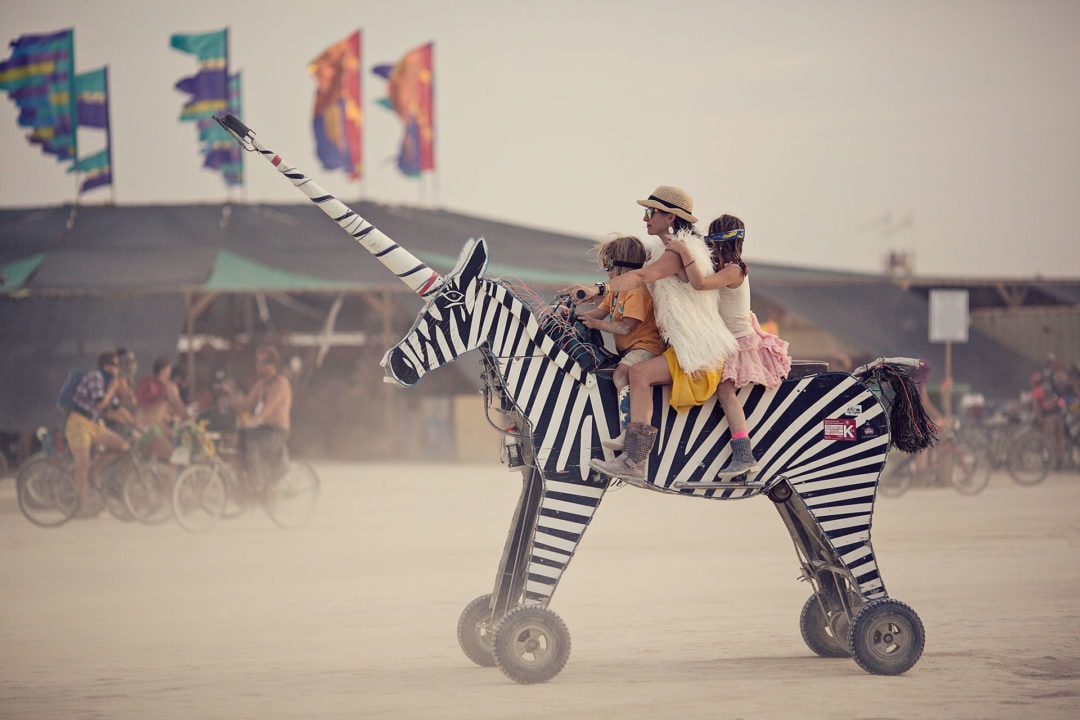 A woman and two children riding a wheeled wooden zebra unicorn.