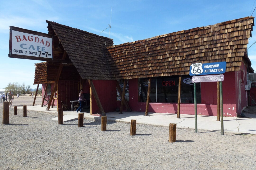 a small red building with a wooden shingle roof in the desert with a sign that says "bagdad cafe open 7 days 7am 7pm", newberry springs california