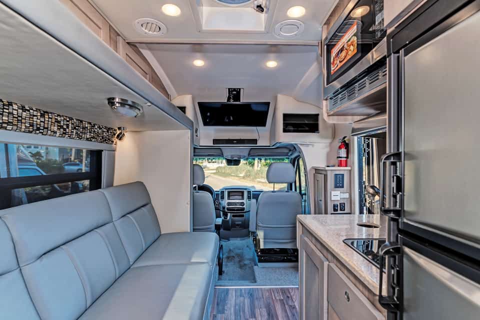 Interior of an RV with kitchen, fridge, seating and driver's cab featured