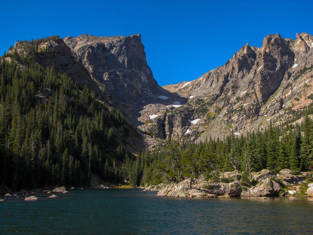 Lake sitting at the foot of a mountain range with trees going up the side of the mountains