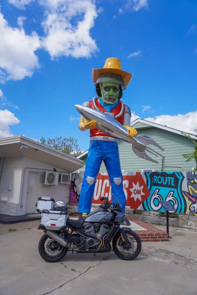 A motorcycle parked in front of a large fiberglass statue of a man holding a rocket ship