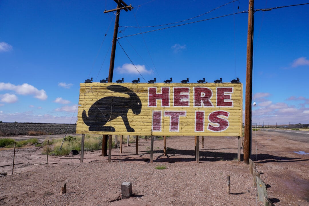 Large yellow billboard with a jackalope silhouette and the words HERE IT IS