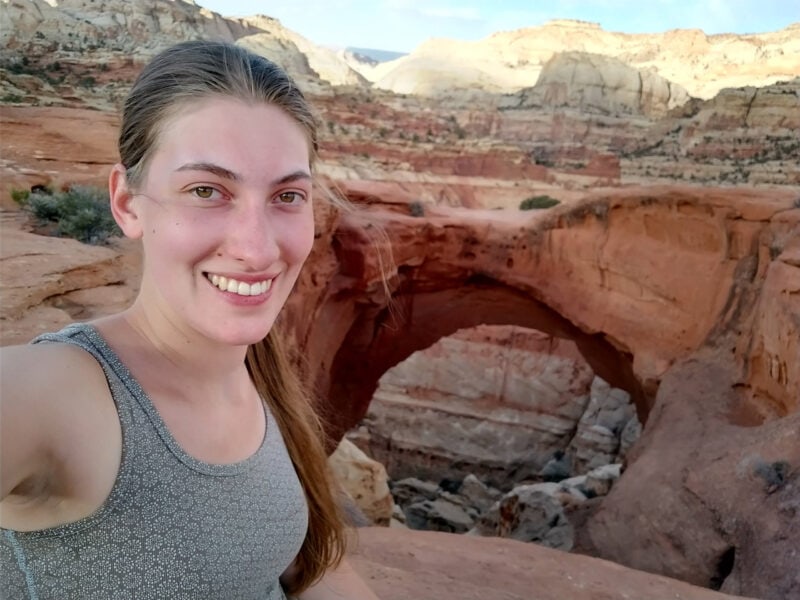 a person takes a selfie in front of a red arch in the desert