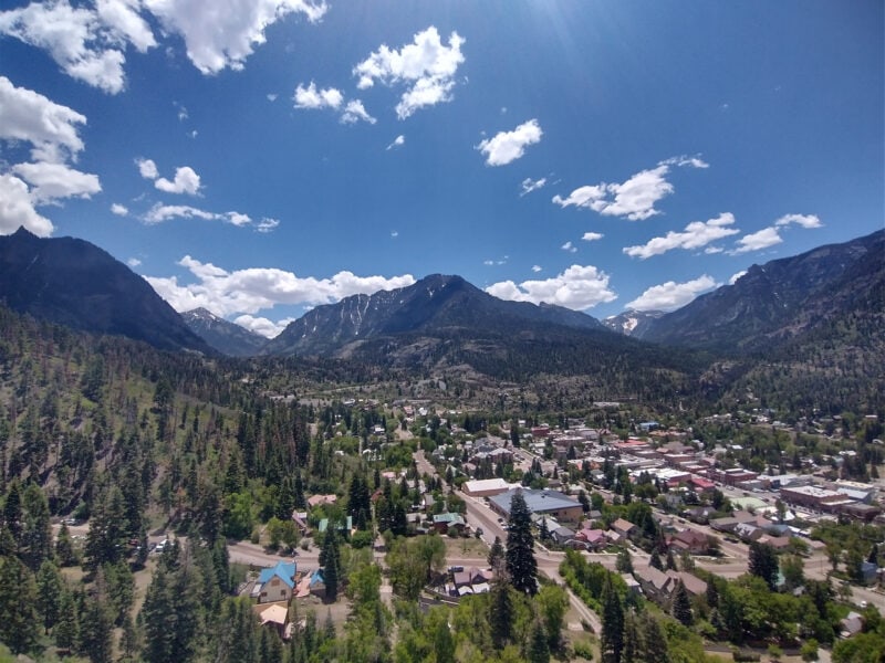 an aerial shot of a town surrounded by mountains under a blue sky