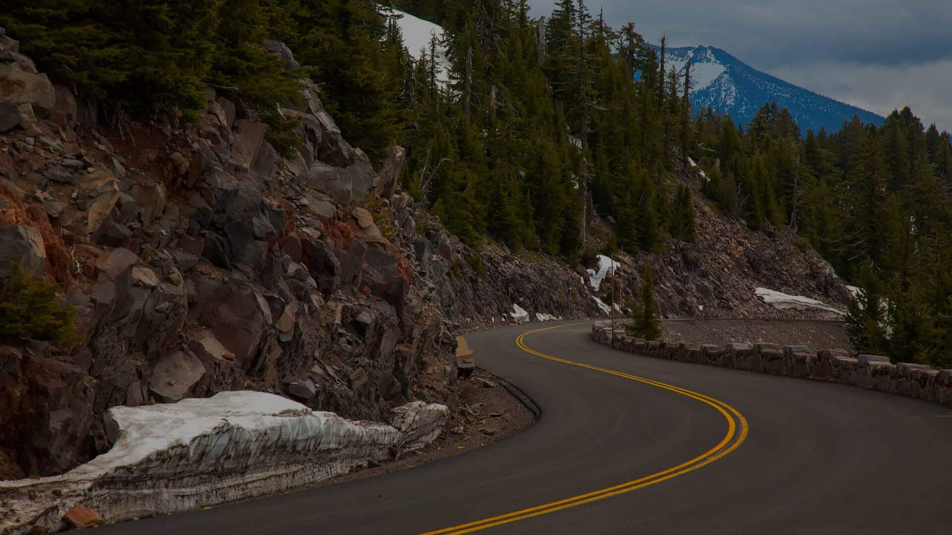 A curved road going through a volcanic, rocky landscape with some snow on the ground