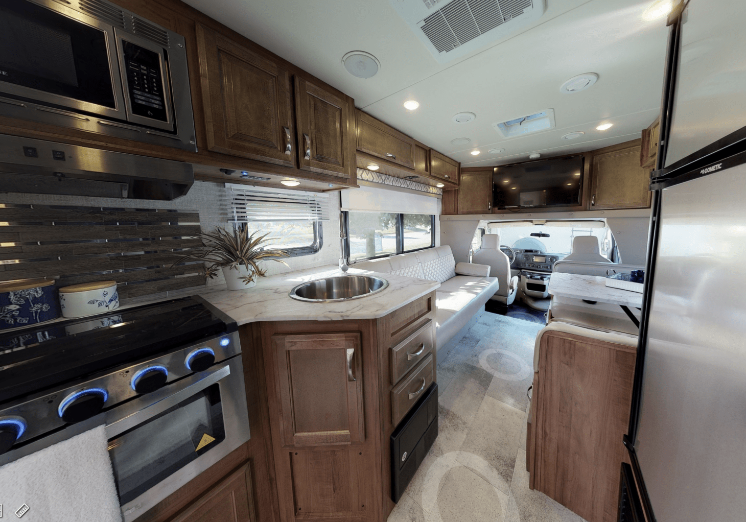 Interior of an RV with a sink, oven, microwave, fridge, dining area, and driver's cab featured